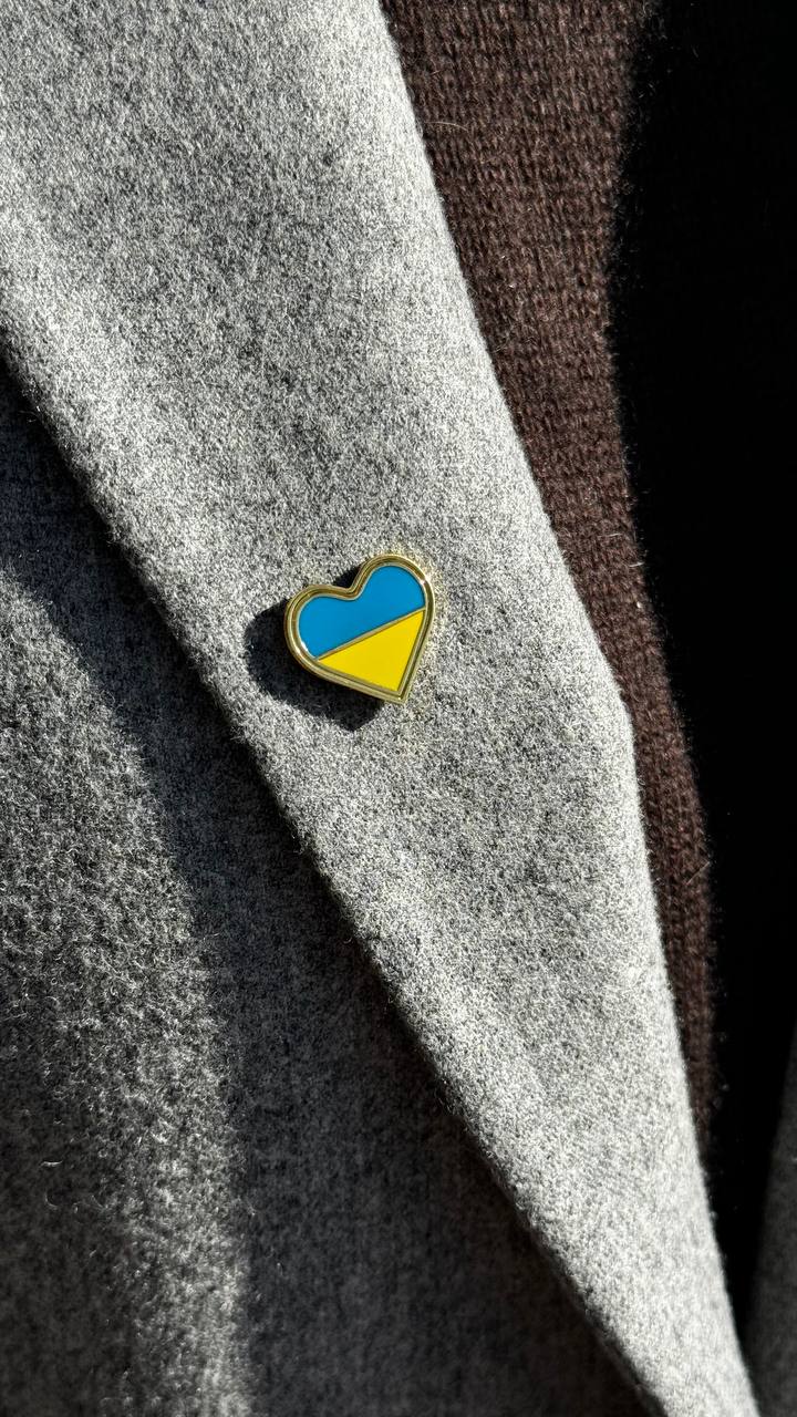 A heart-shaped badge with Ukrainian flag colors attached to a grey fabric.