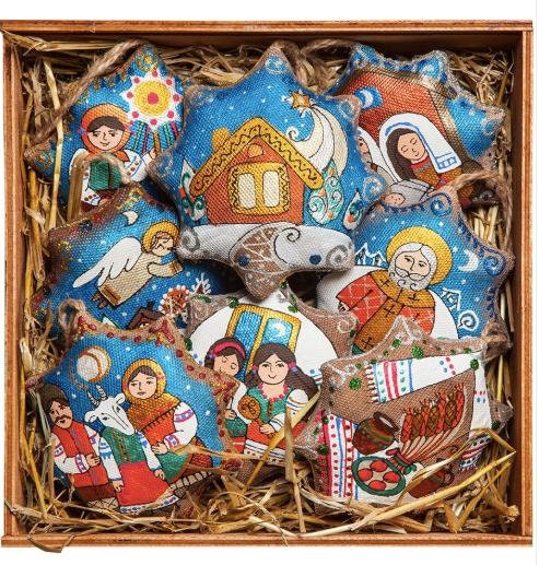 A set of decorated star-shaped Christmas tree ornaments displayed in a wooden box, filled with straw. The ornaments are adorned with traditional Ukrainian festive designs.