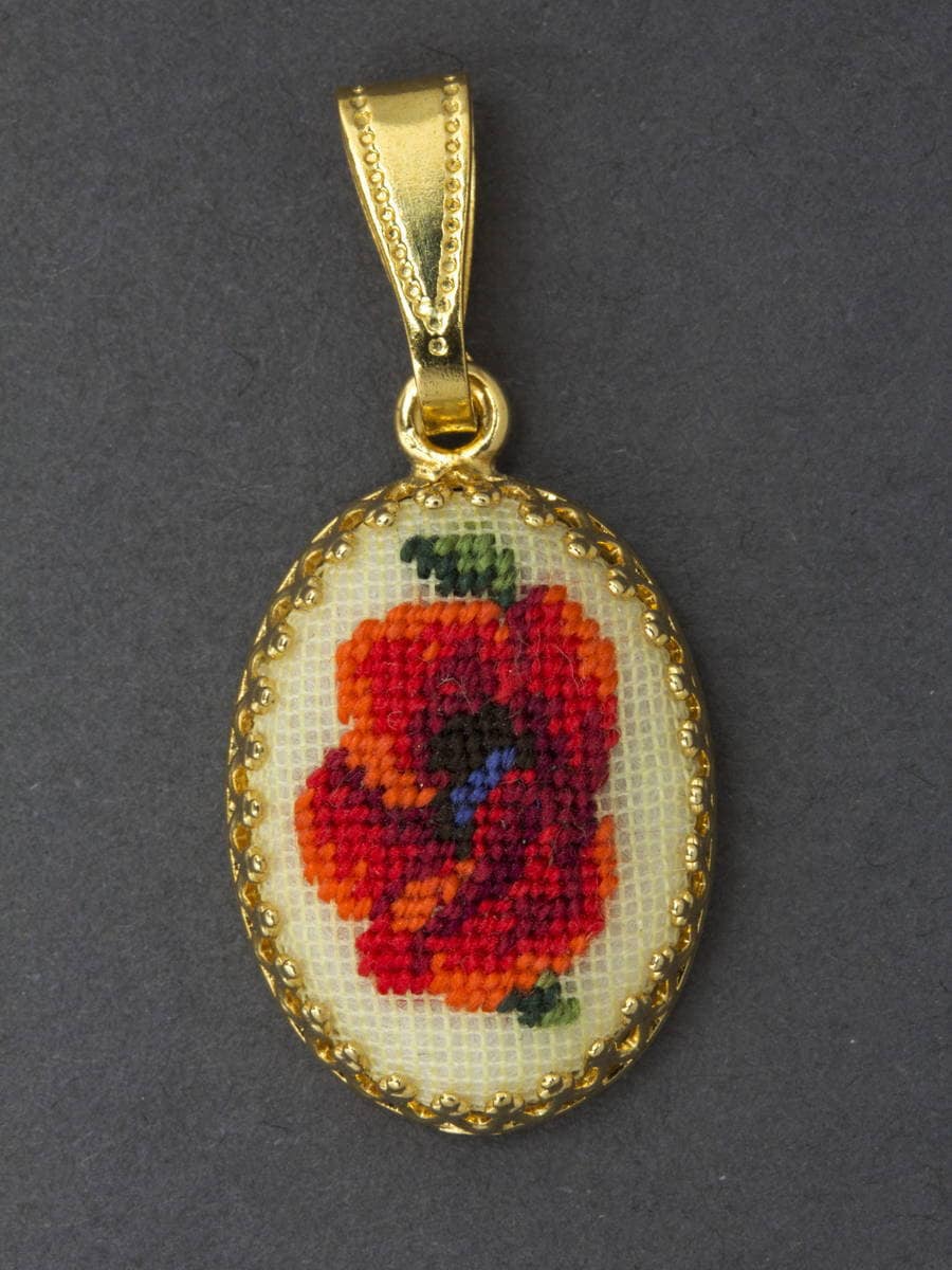 An oval-shaped embroidered pendant necklace with a floral design, predominantly red, on a white background with a gold-colored frame