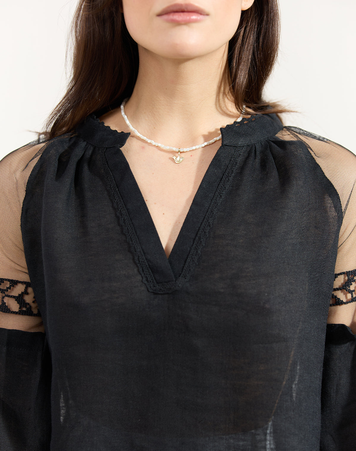 Black blouse with sheer sleeves and neckline, worn by a person.