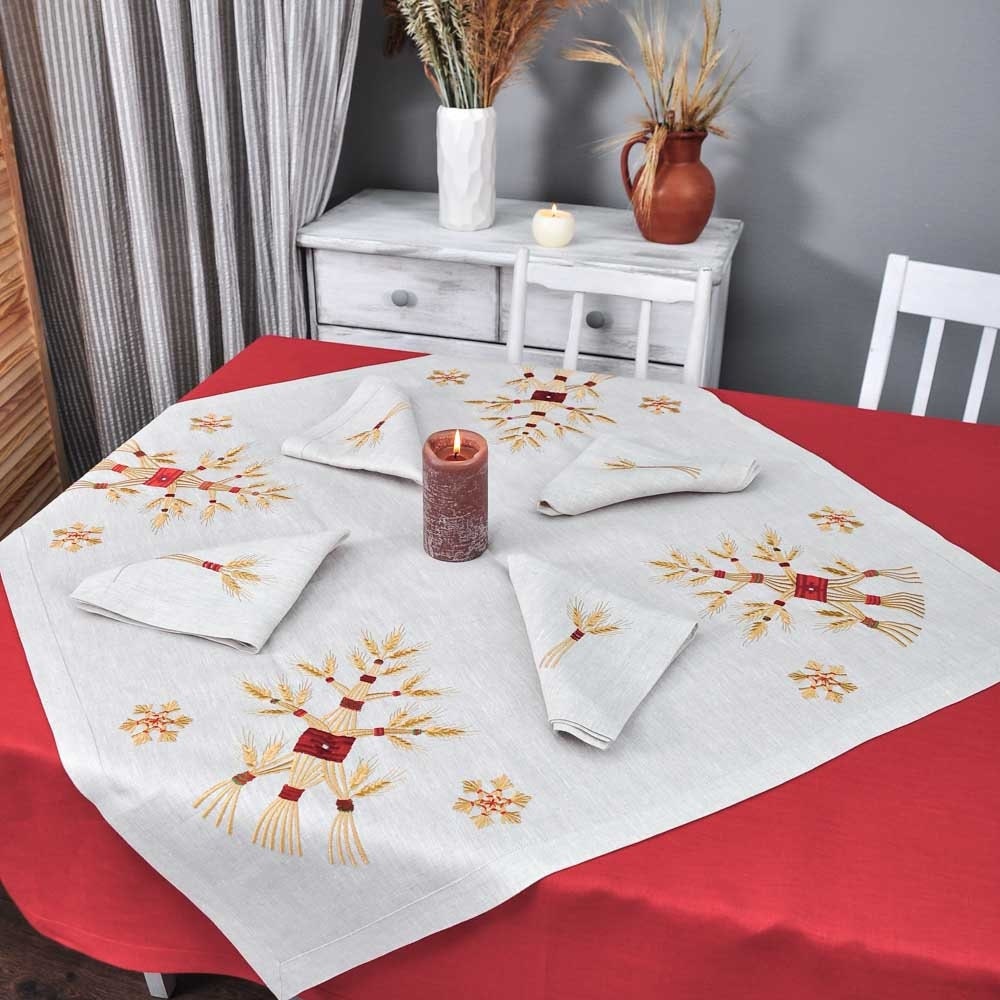 An embroidered white tablecloth with red and gold accents displayed on a table, accompanied by two matching napkins folded neatly.