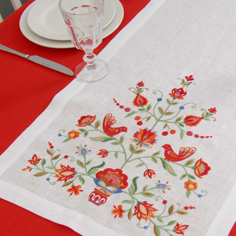 Embroidered tablecloth with floral and bird design on a red tablecloth.