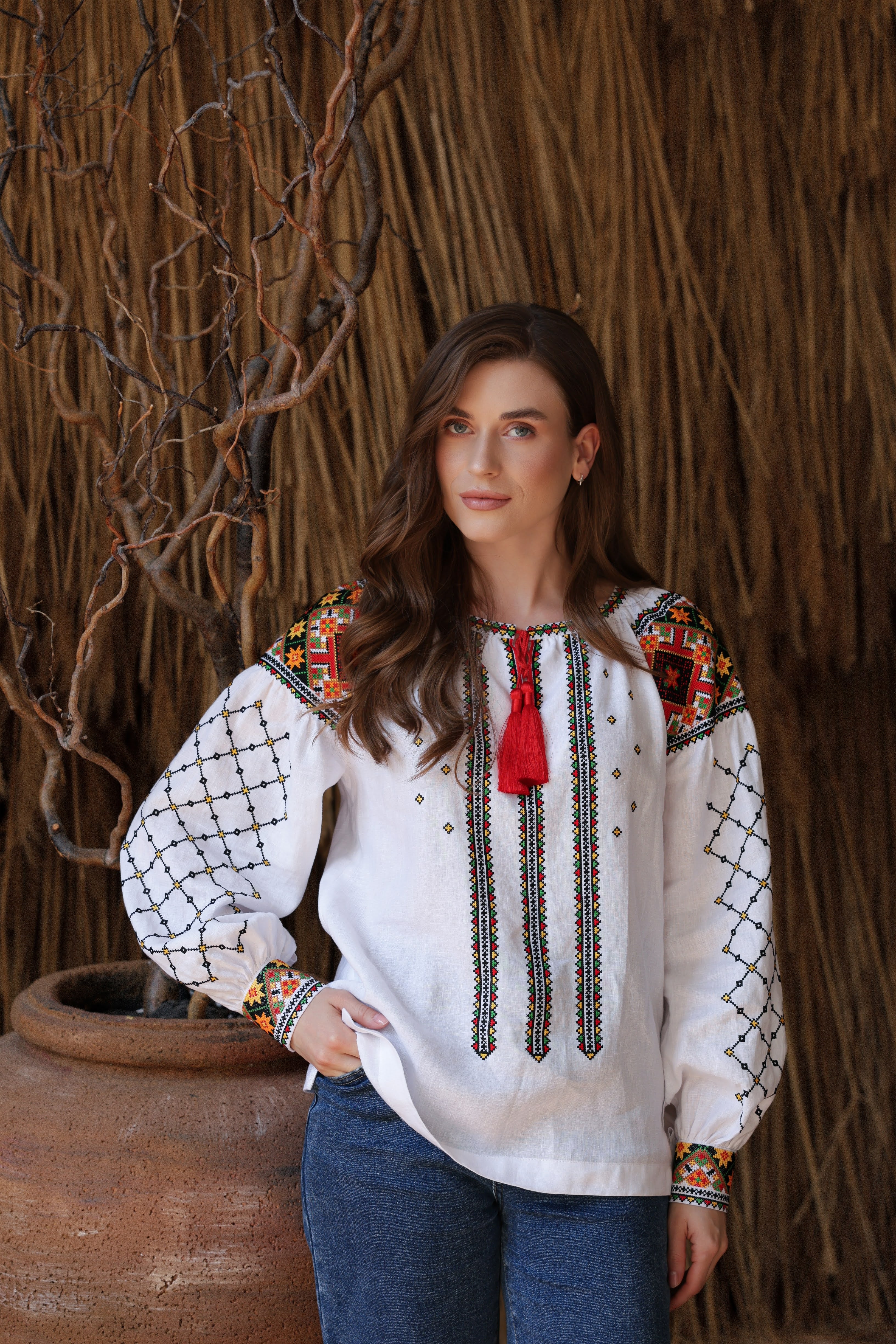 Woman wearing a traditional embroidered blouse with a red tassel against a rustic background