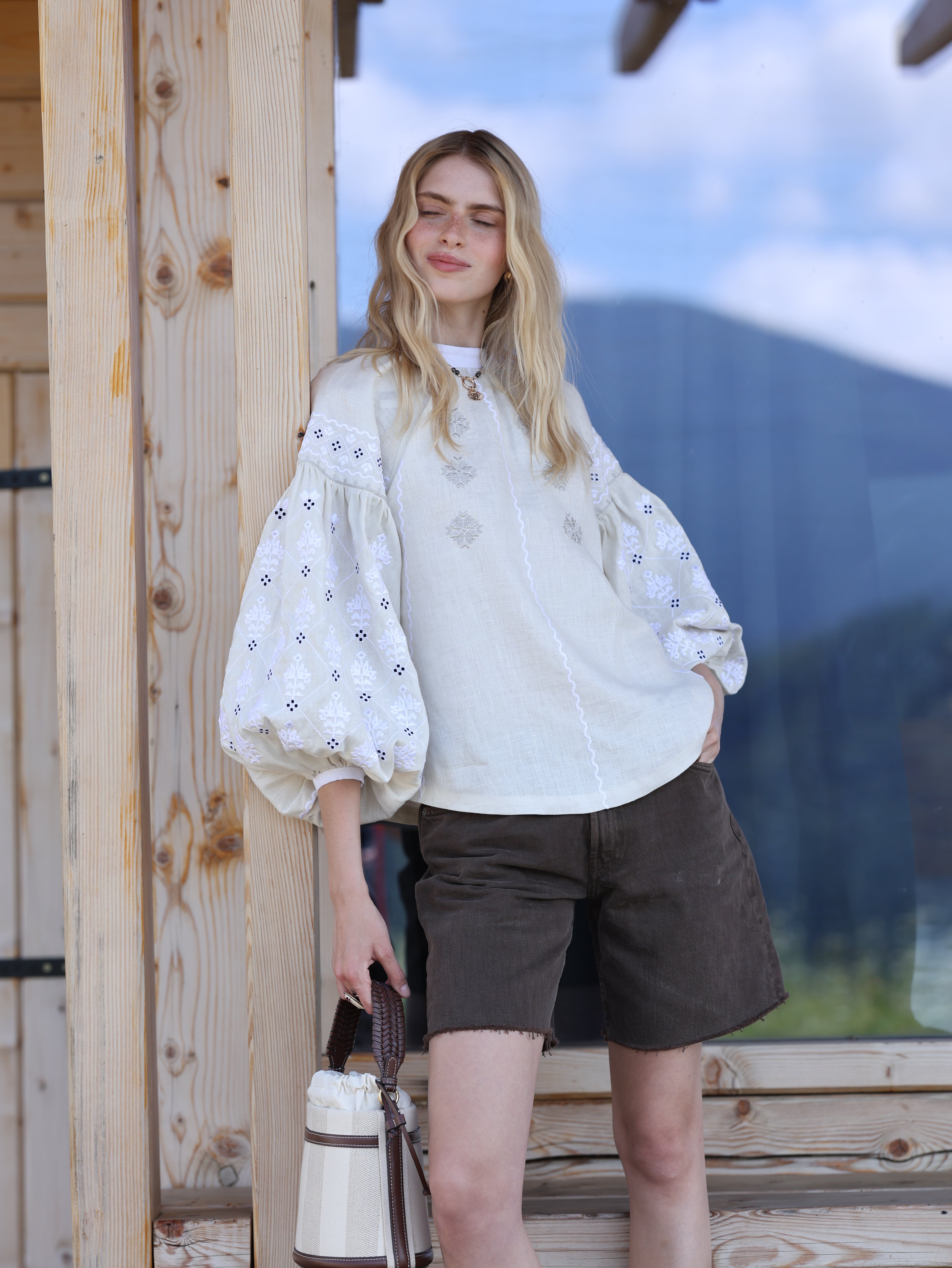 Woman in a white blouse with puffed sleeves standing on a wooden platform.