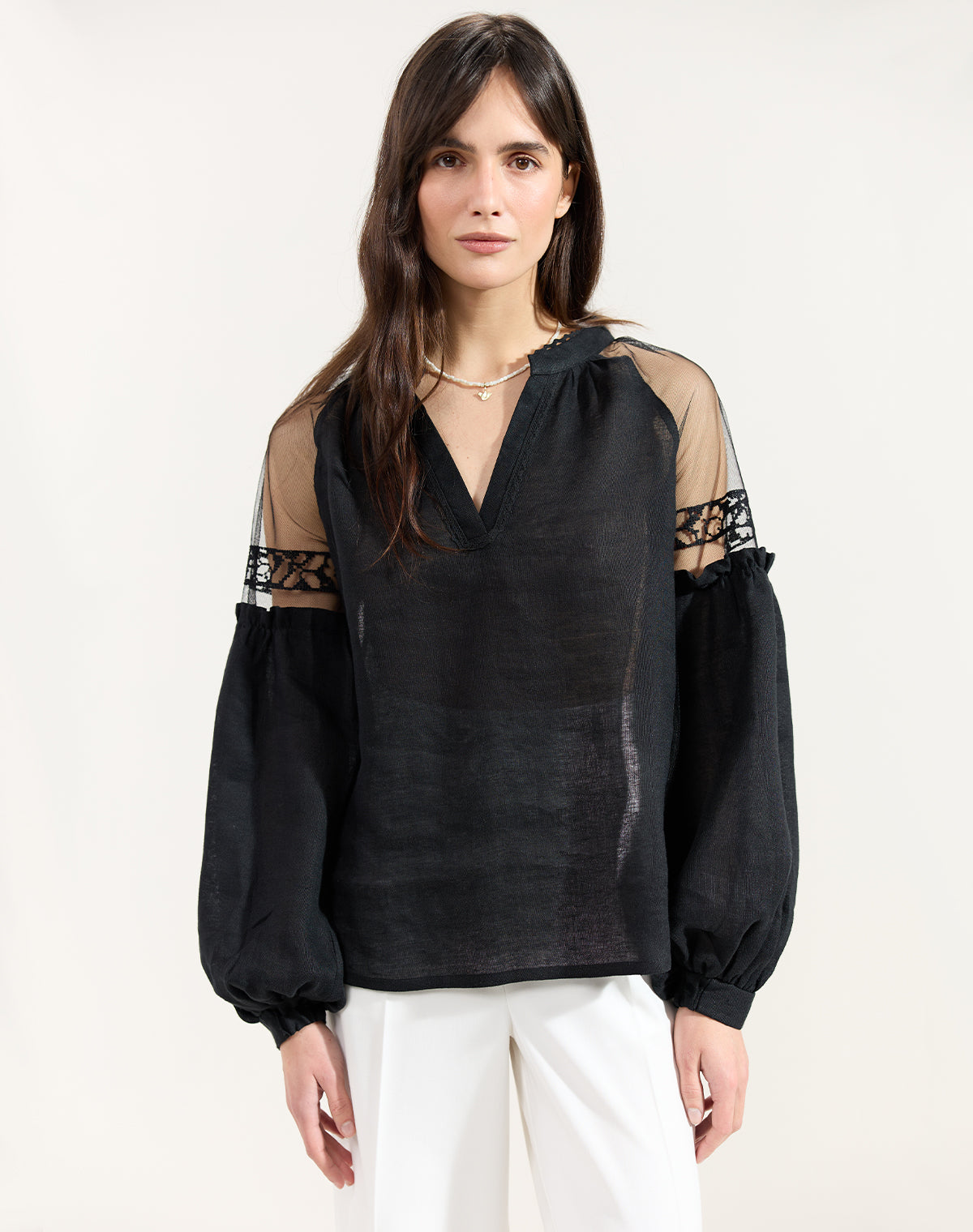 Woman wearing a black blouse with sheer sleeves on a white background