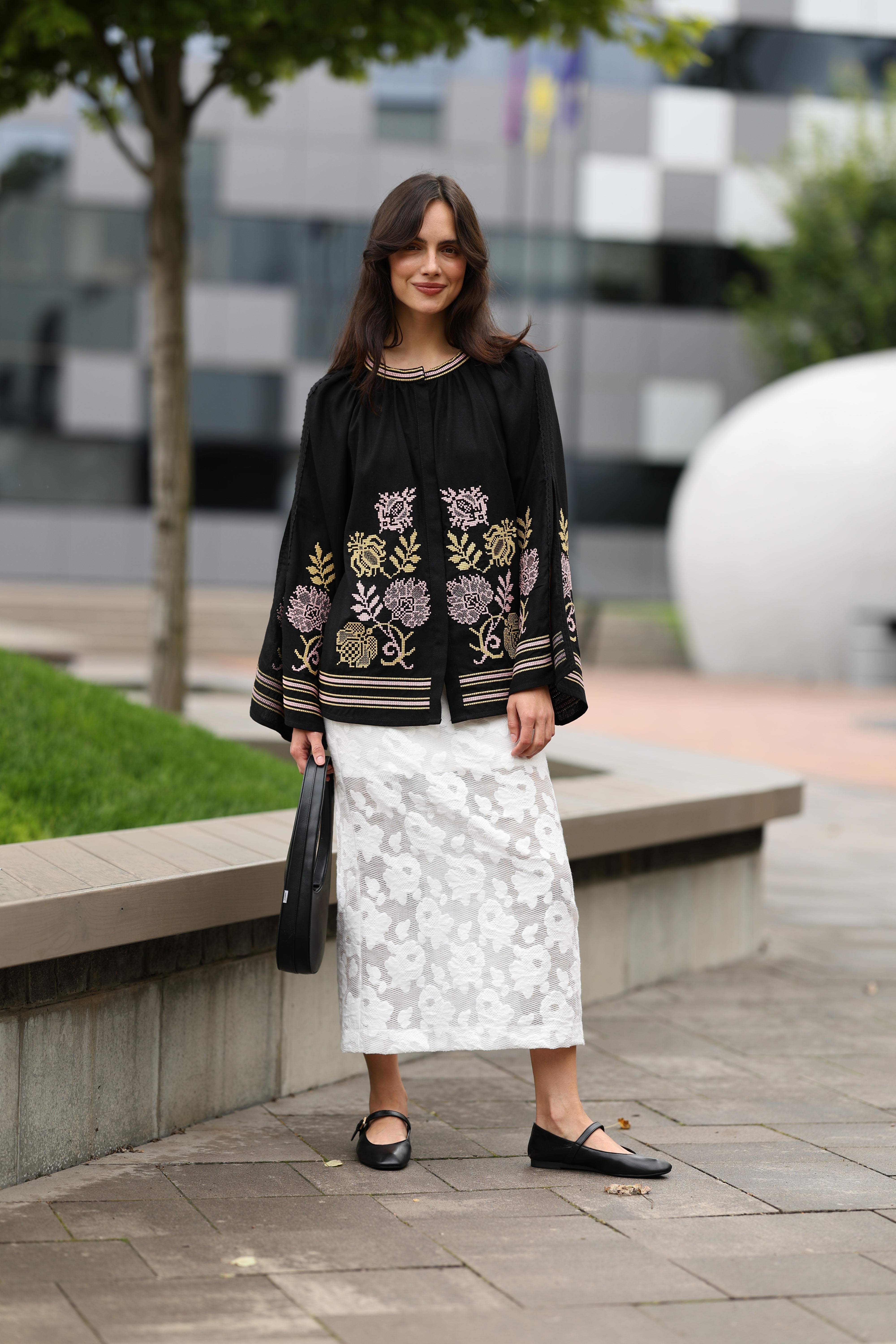 Woman wearing a black embroidered top and white lace skirt in an urban setting