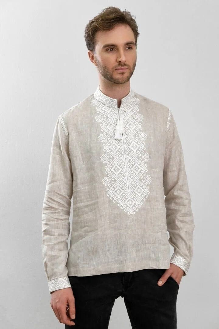 A man wearing a beige linen vyshyvanka shirt with white embroidery, featuring a geometric pattern.