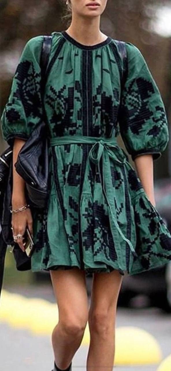 A woman wearing a green linen embroidered Ukrainian boho vyshyvanka dress with black patterns, featuring a round neckline and short sleeves.