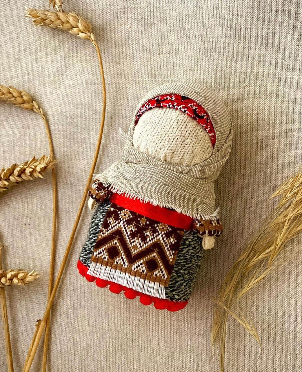 A handmade Ukrainian Motanka doll with a traditional geometric pattern, dressed in a girl's outfit, and adorned with a decorative red and white striped bandana.