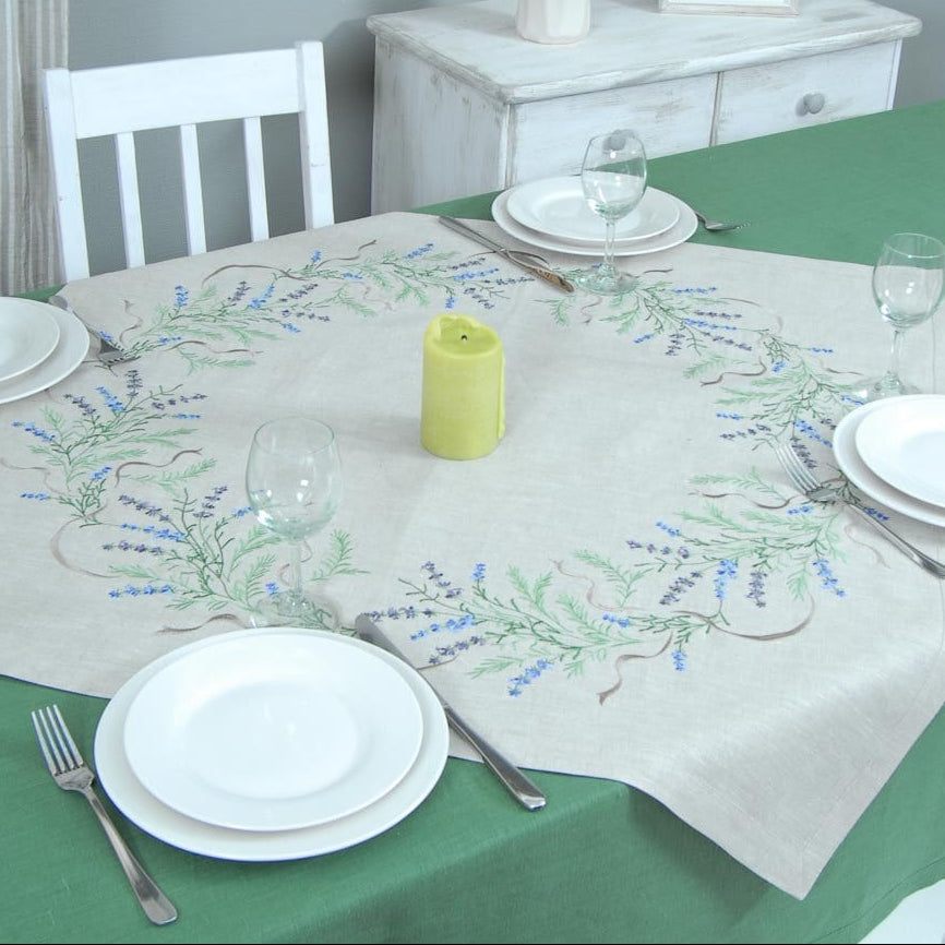 A linen tablecloth with embroidered lavender designs displayed on a table with dishes and a green tablecloth.