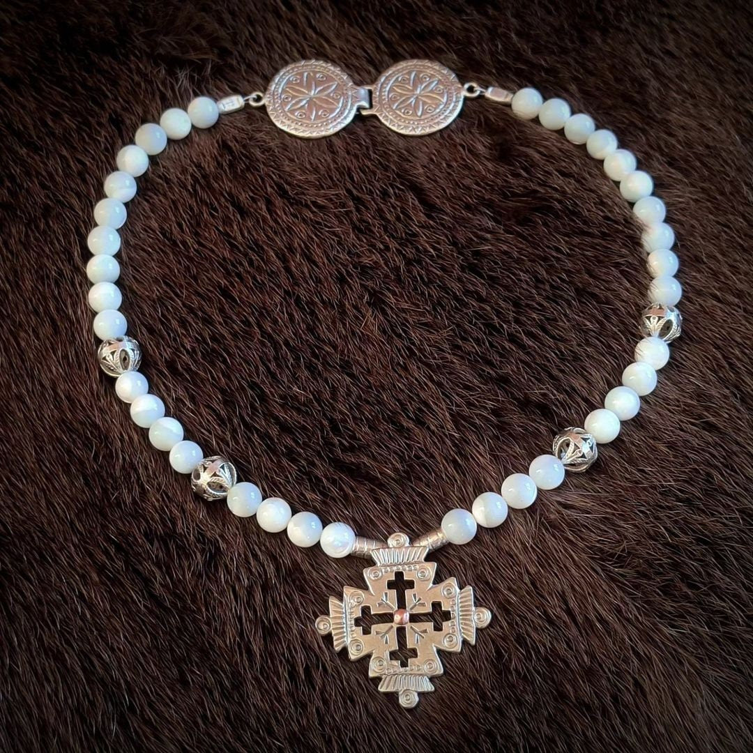 A silver-colored metal necklace featuring a cross pendant and bead embellishments, displayed against a furry dark background.
