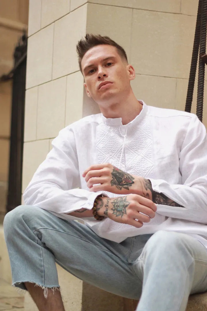Man wearing a white shirt and light blue jeans sitting on a stone bench.