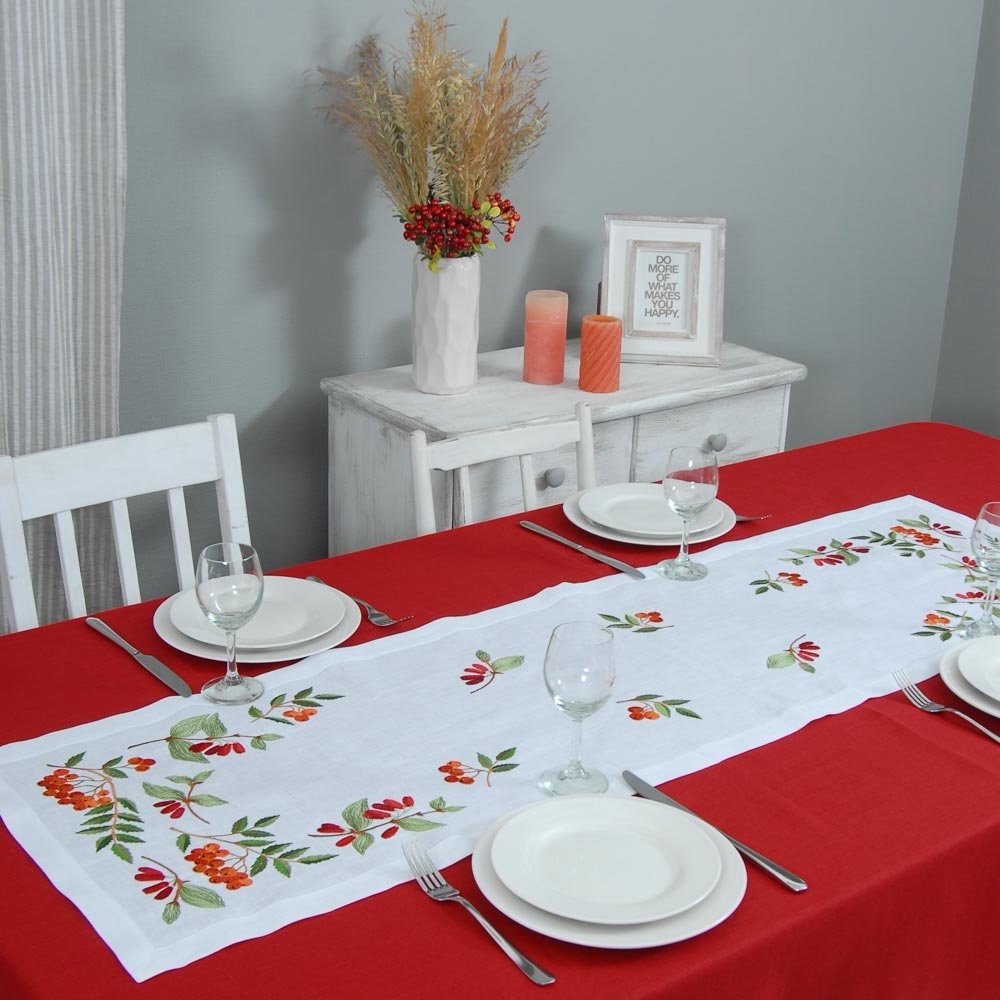 white linen tablecloth and four napkins with embroidered red and green floral patterns
