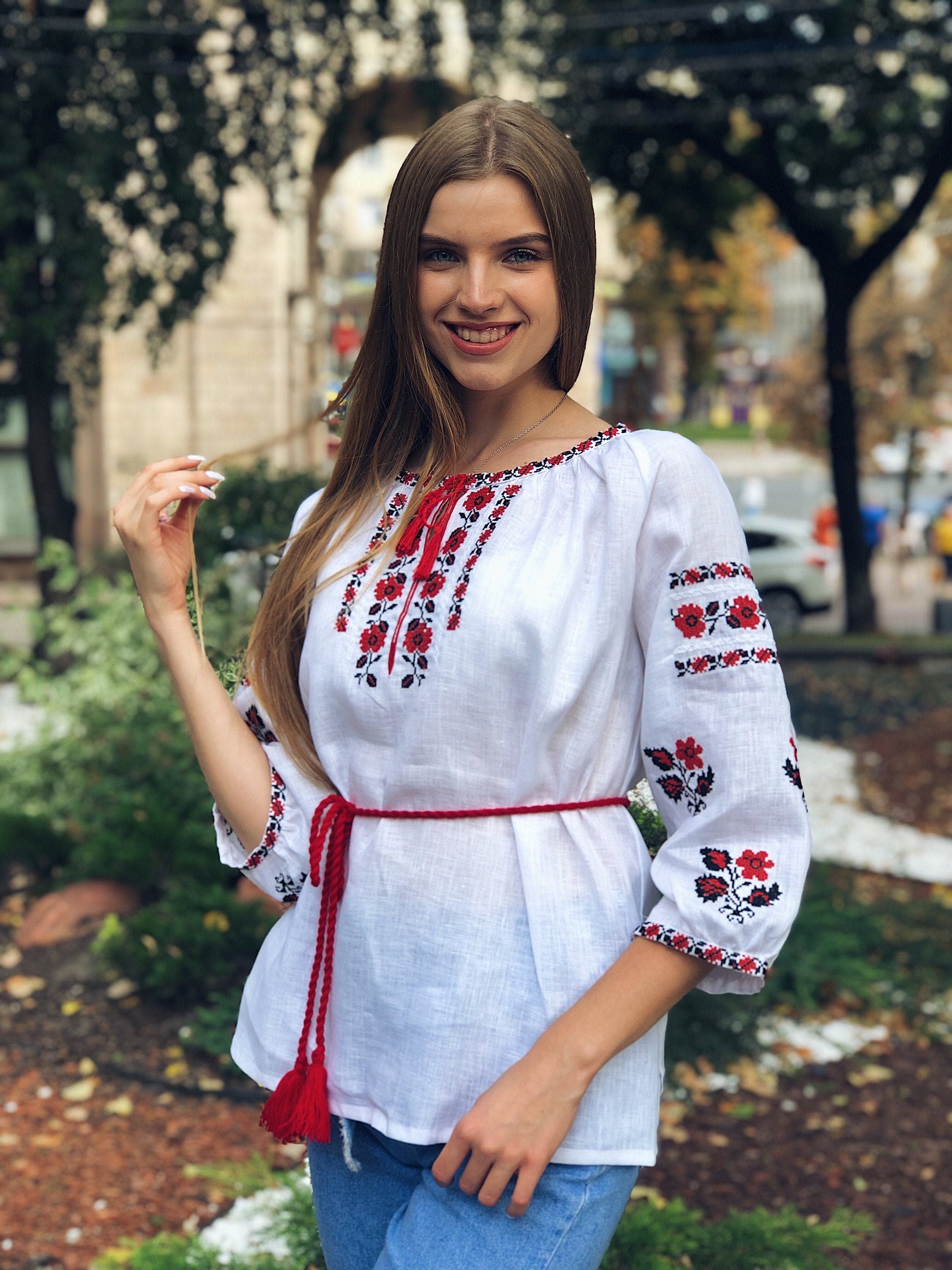 A woman wearing a white linen vyshyvanka blouse with red embroidered details and a red sash.