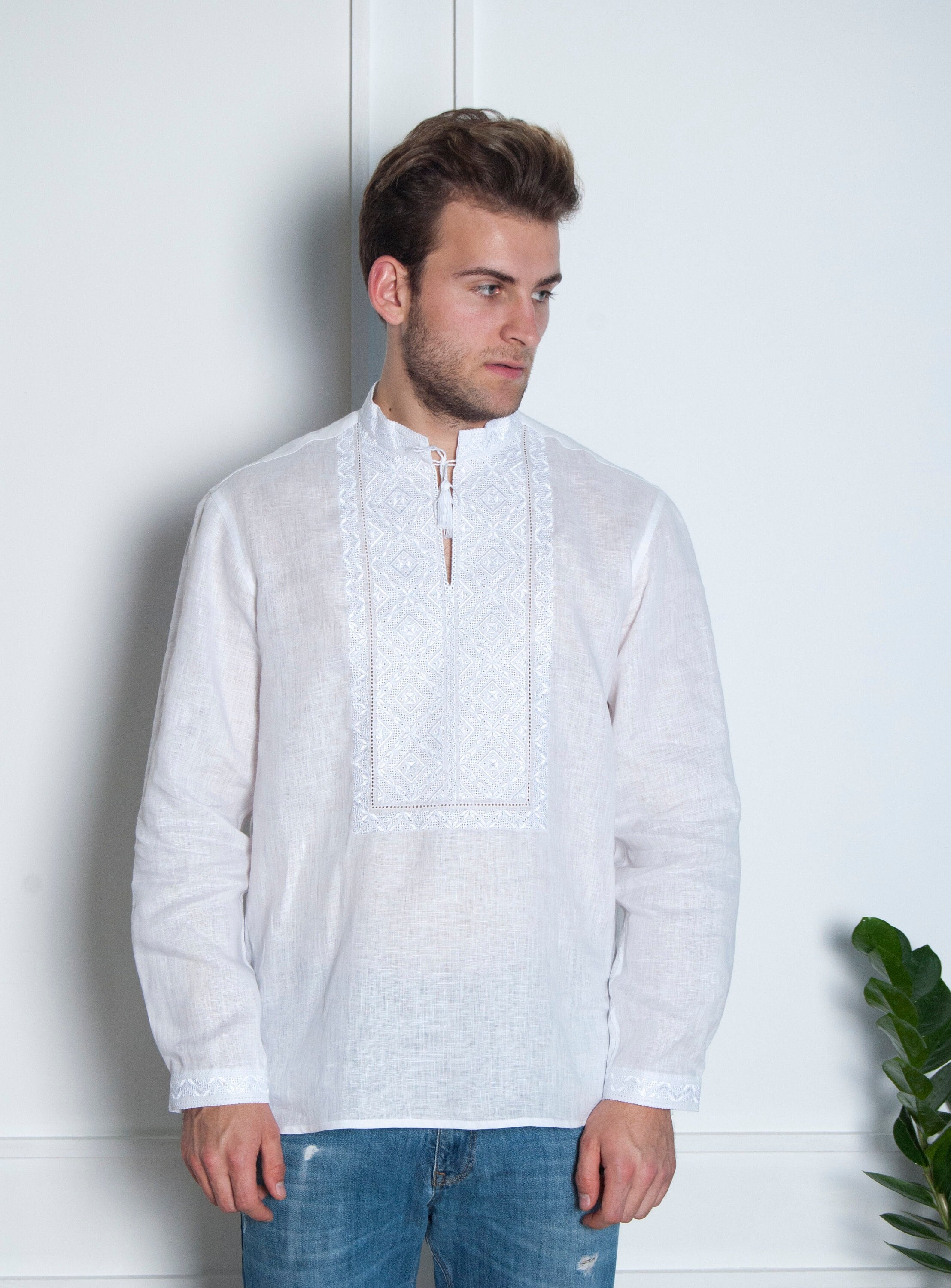 A man wearing a white long-sleeved embroidered shirt with a round neckline.