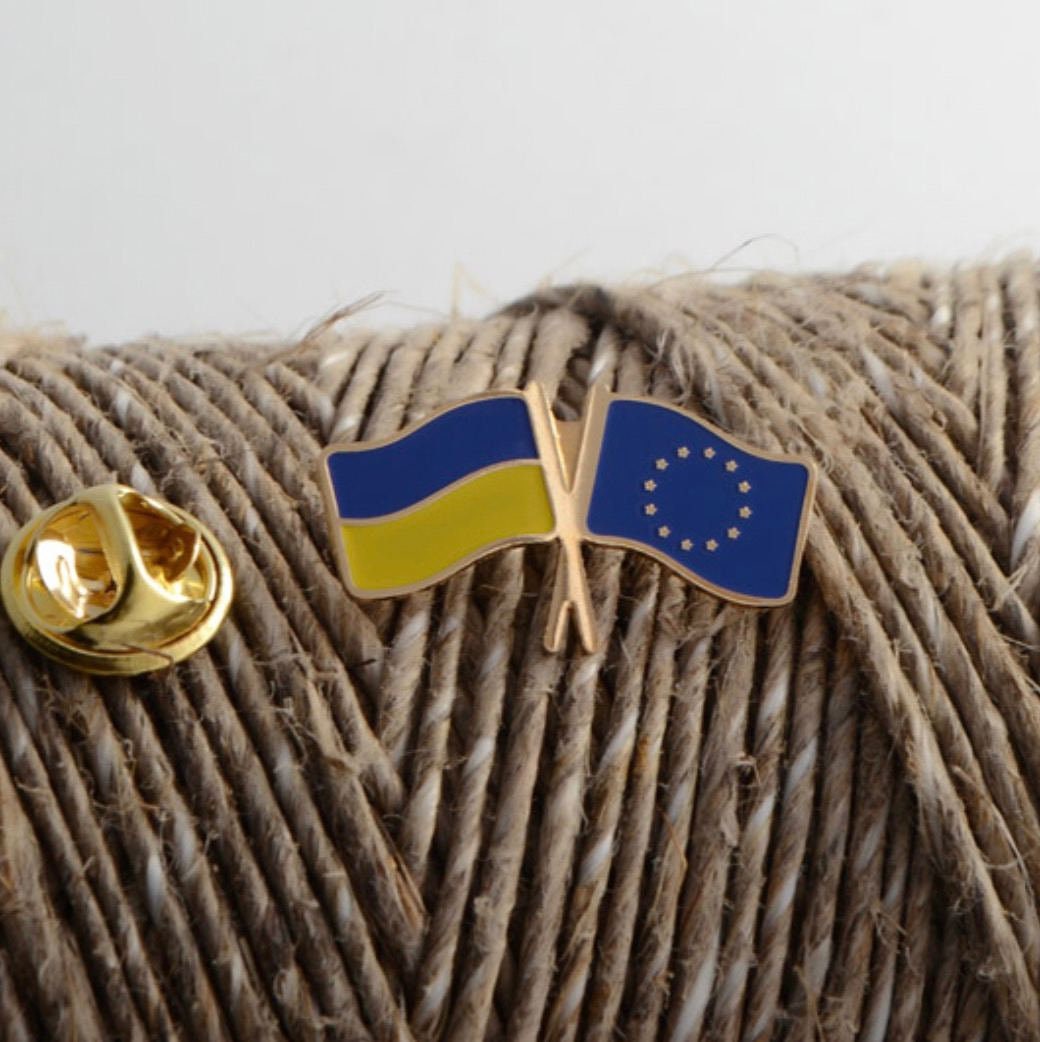 A brass badge featuring the Ukrainian flag and the European Union flag placed on a spool of twine.