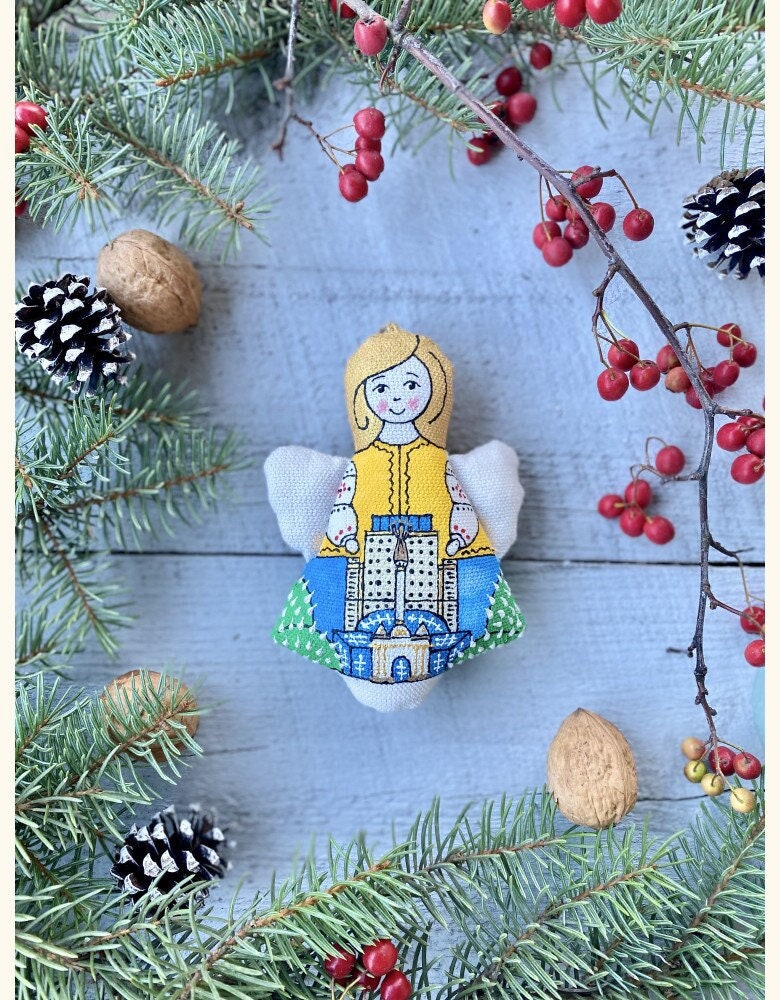 A handcrafted fabric angel toy with a yellow dress, sitting amidst festive decorations like pine cones and red berries.
