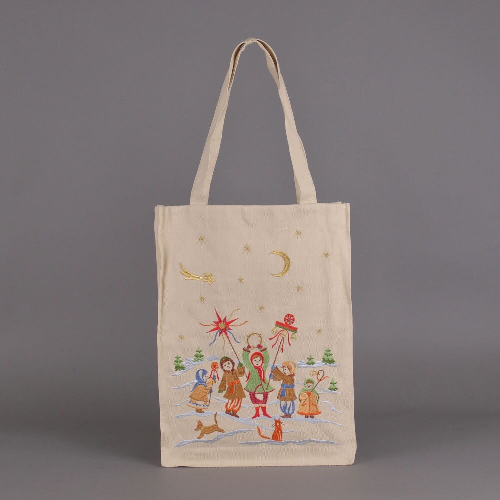 A linen shoulder bag with embroidered decoration featuring Christmas carol singers and festive motifs on a light background.
