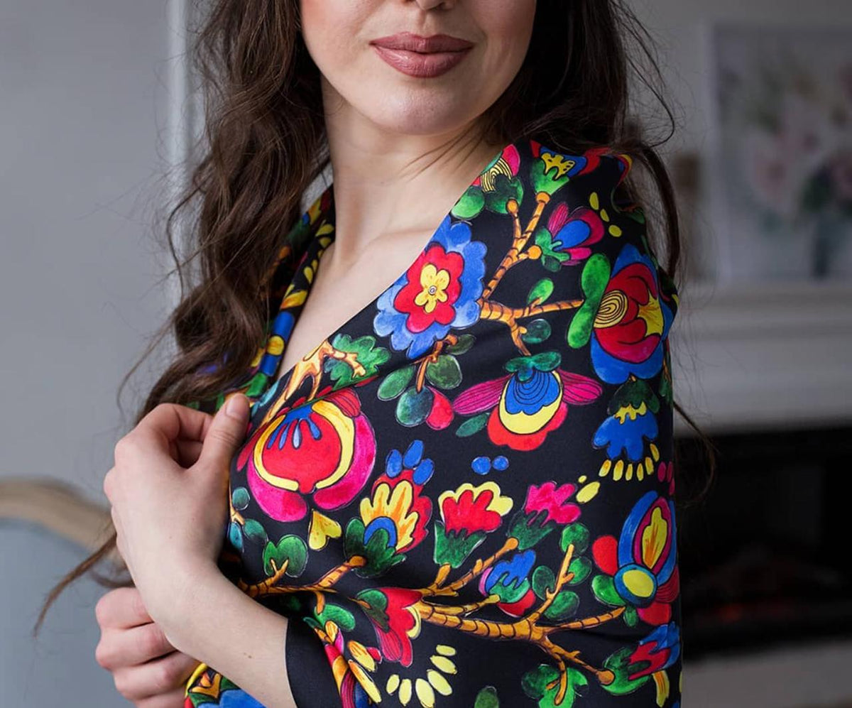 A close-up of a woman wearing a black wrap-style top with a vibrant, multicolored floral and folk-art style print in red, blue, yellow, green, and orange.