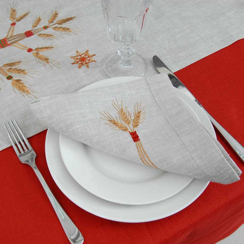 A linen napkin with embroidered Ukrainian patterns is placed on a plate on a red tablecloth, part of a set of tableware.
