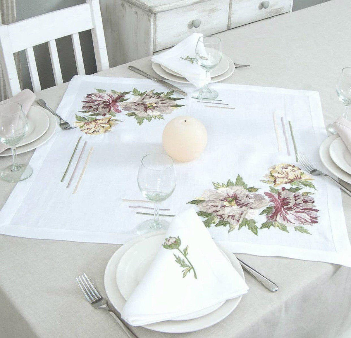 A linen tablecloth with embroidered peony designs, displayed on a table with dishes and silverware.