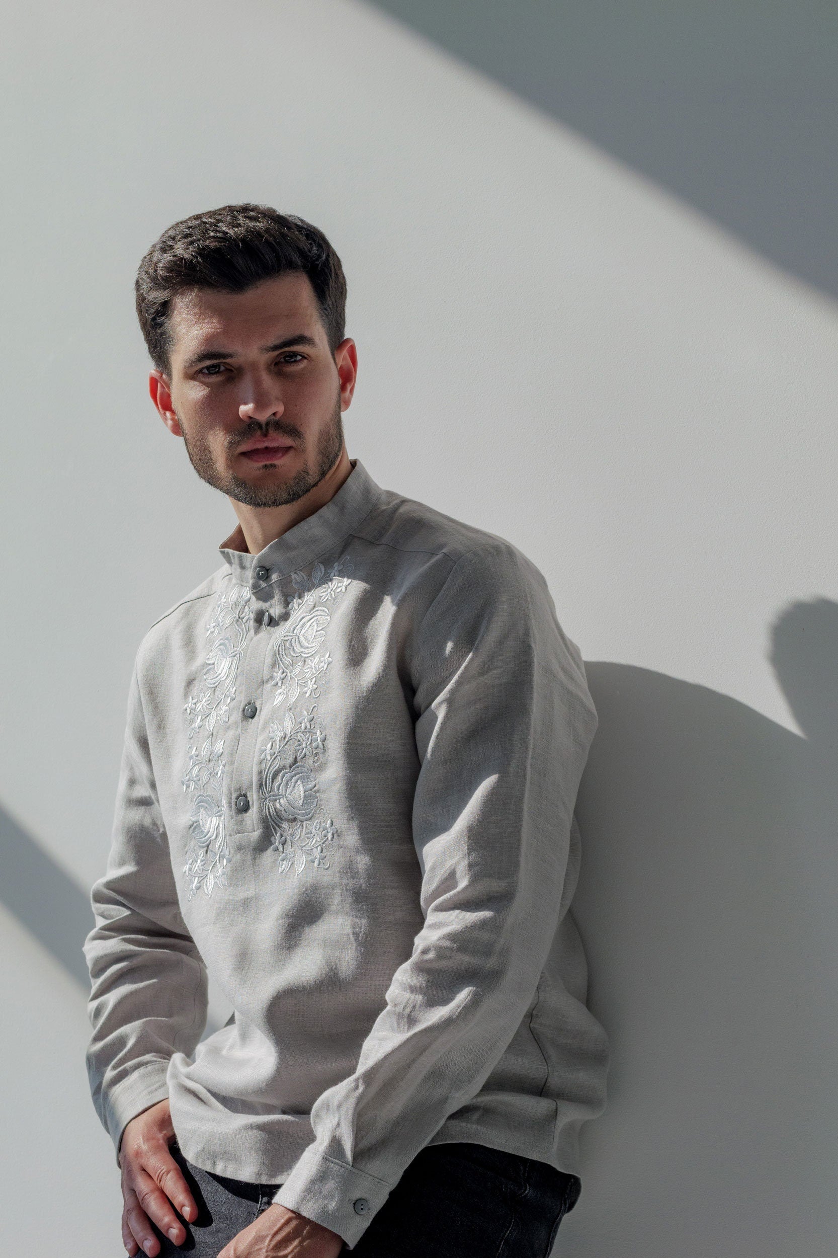 A man wearing a long-sleeved men's grey linen vyshyvanka shirt with white embroidery, standing against a white background.