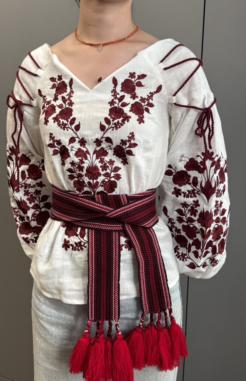 White blouse with red floral embroidery and a matching belt on a neutral background