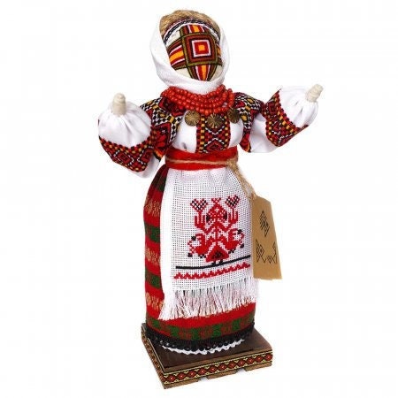 Ukrainian handcrafted Motanka doll, wearing traditional dress with red and white embroidery, displayed on a wood stand.