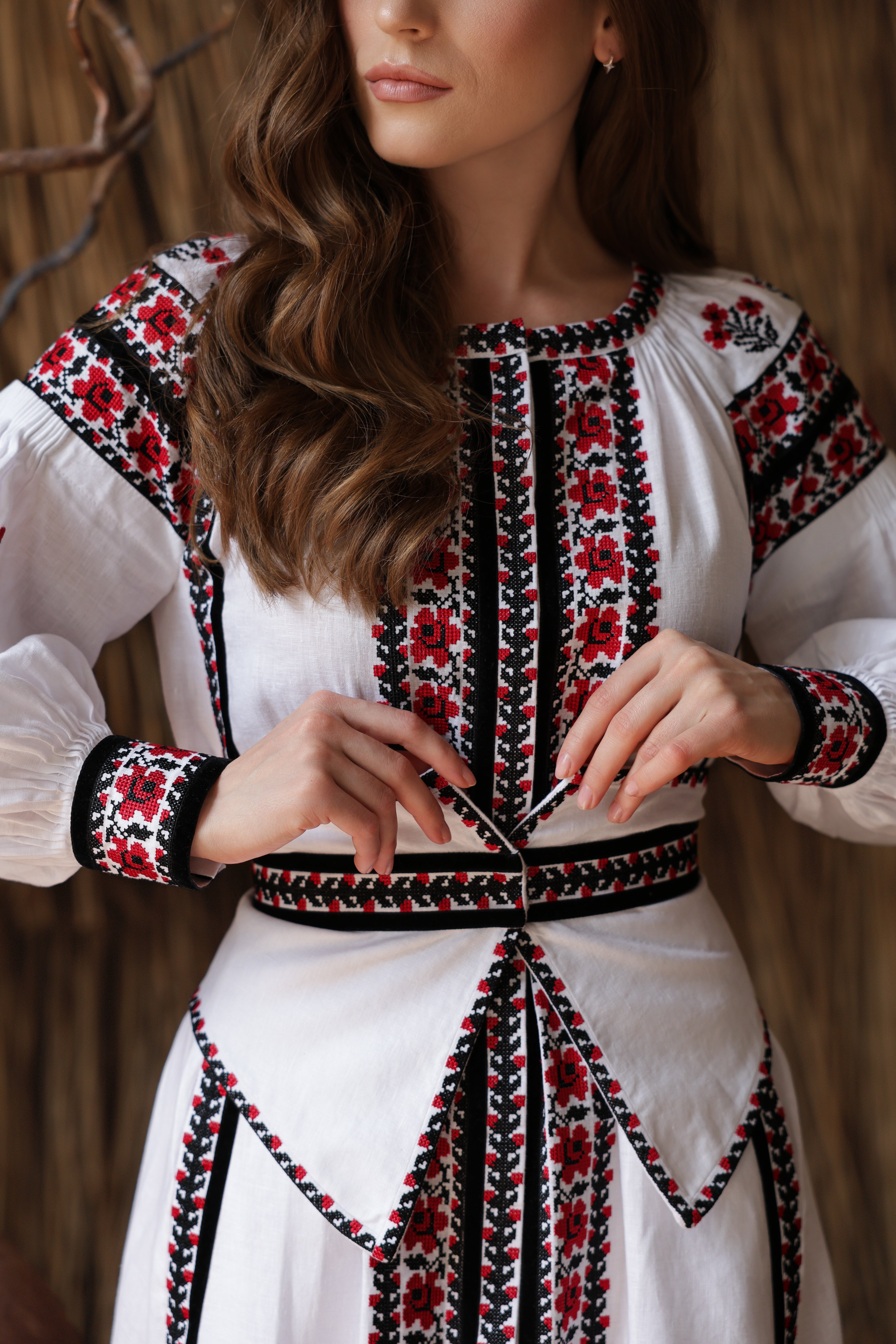Woman wearing a white dress with black and red embroidery against a wooden background