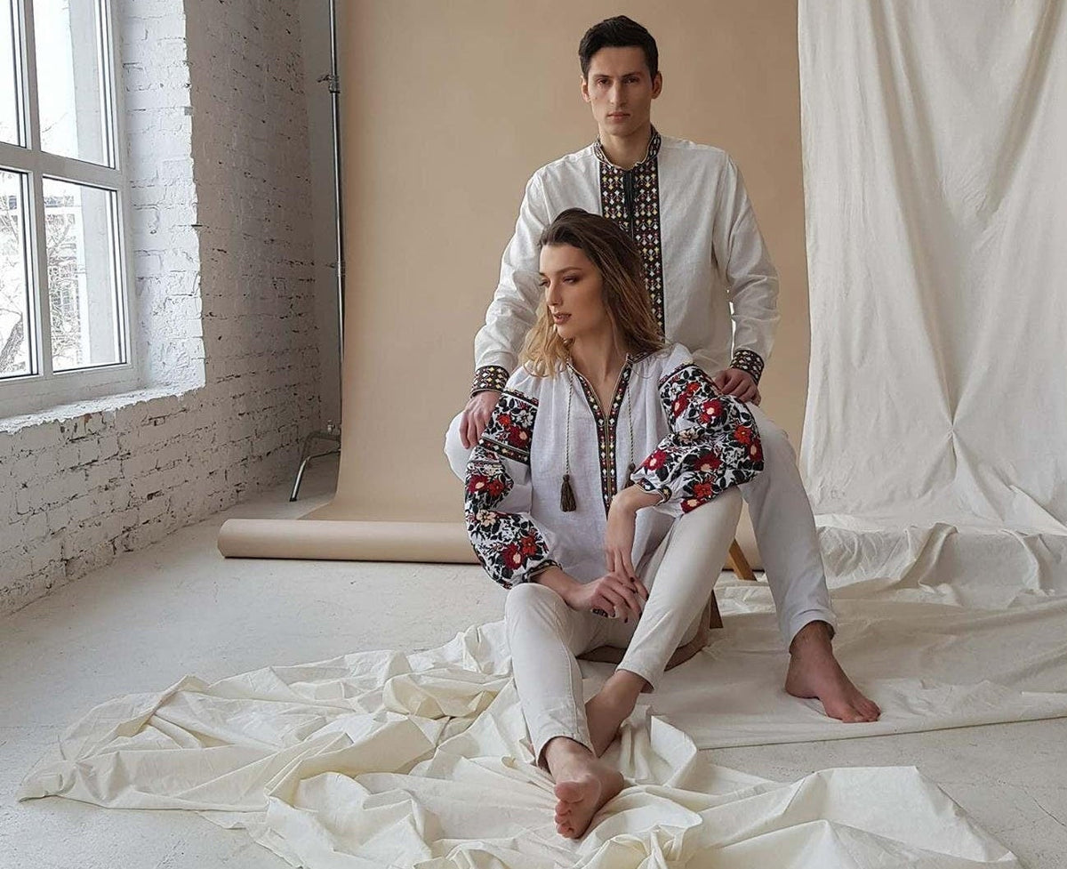 Two people sitting on a white fabric in a studio setting with a large window and white walls.