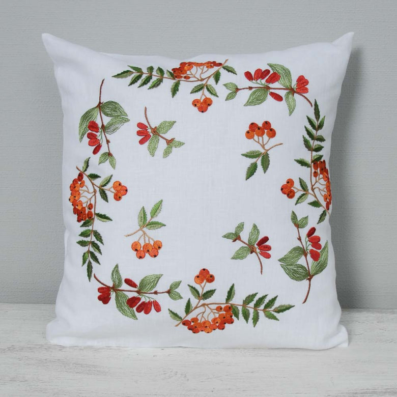 White pillow with embroidered red and green floral pattern on a gray background