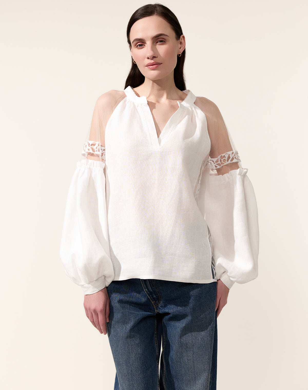 Woman wearing a white blouse with lace sleeves against a plain background