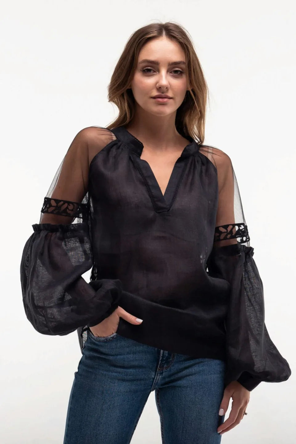 Woman wearing a black blouse with sheer sleeves and blue jeans on a white background
