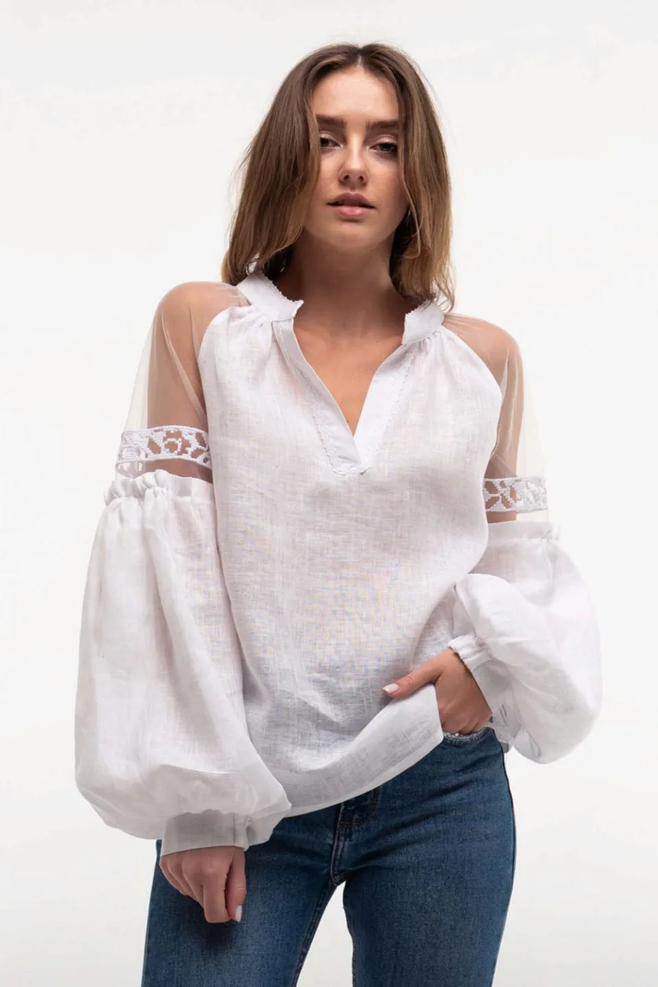 Woman wearing a white blouse with sheer sleeves and blue jeans on a white background