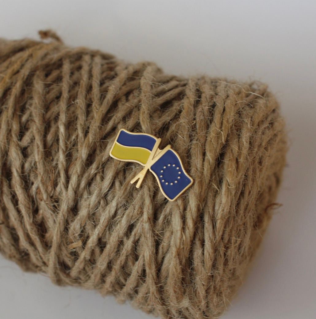 A brass badge featuring the Ukrainian flag and the European Union flag placed on a spool of twine.