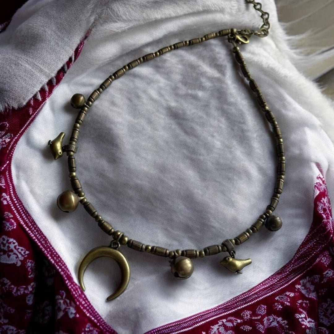 A bronze metal necklace with geometric pendants laid out on a white furry surface, with elements of traditional Ukrainian folk art.