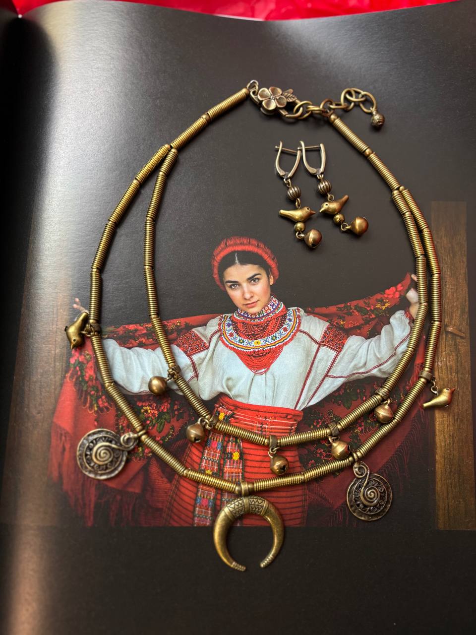 Gold necklace with various pendants on a book with an illustration of a woman in traditional attire.