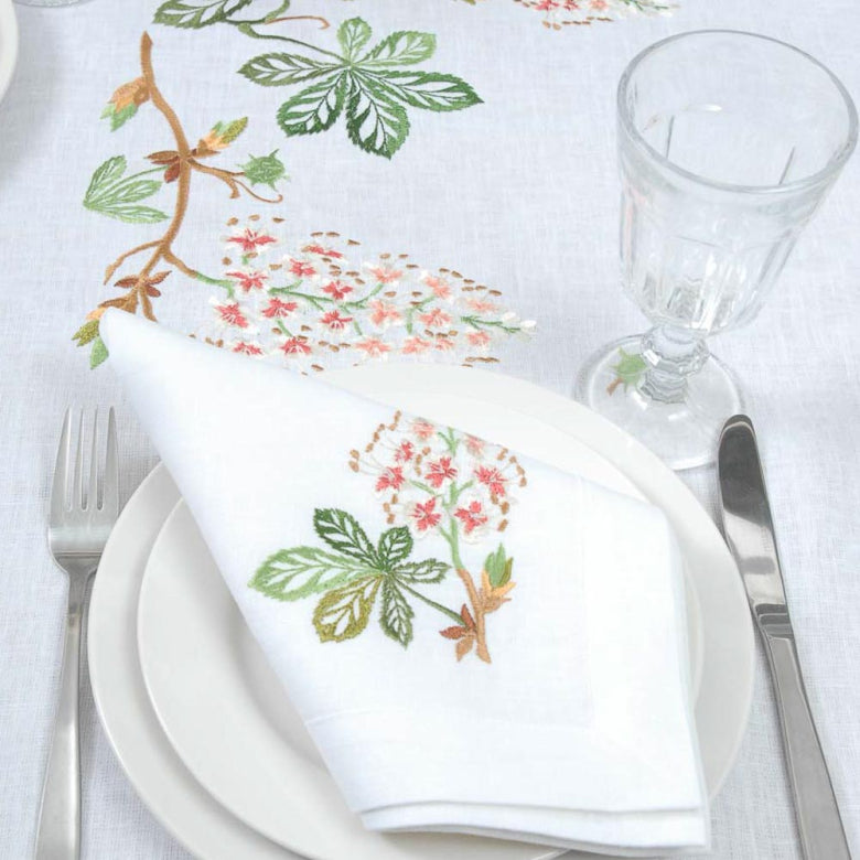 Table setting with floral embroidered napkin, plate, and glass on a white tablecloth.