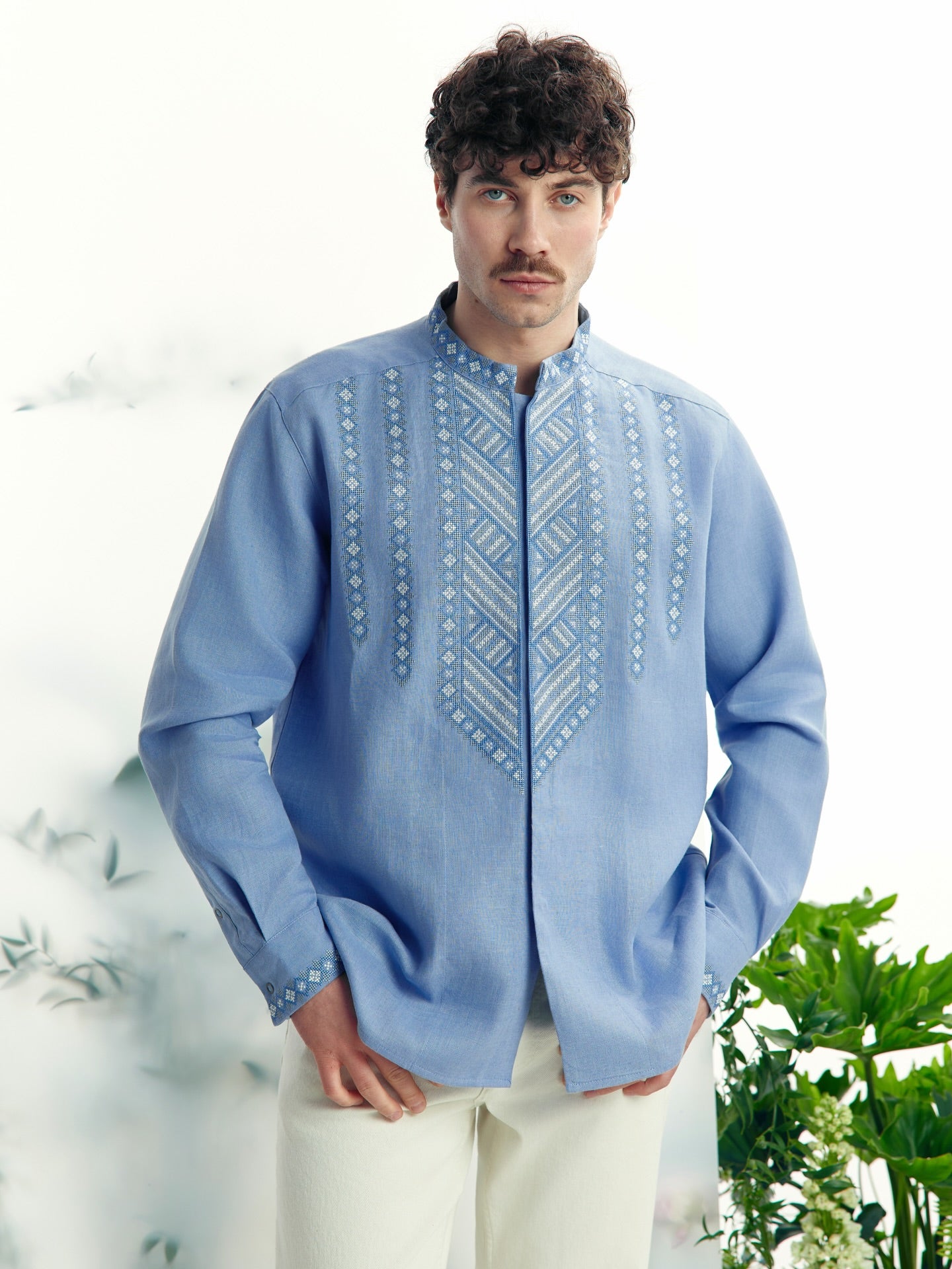 Man wearing a light blue embroidered shirt with a white background