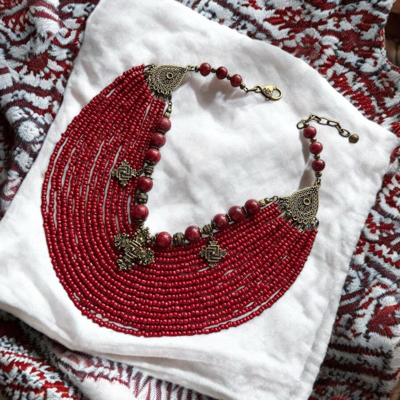 A multicolored beaded necklace with brass pendants laid out on a white fabric, with patterns suggesting a traditional Ukrainian design.