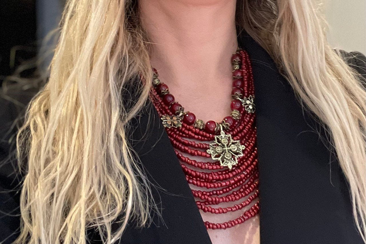 A close-up image of a red necklace with bronze accents and large glass beads worn by a person with long blonde hair.