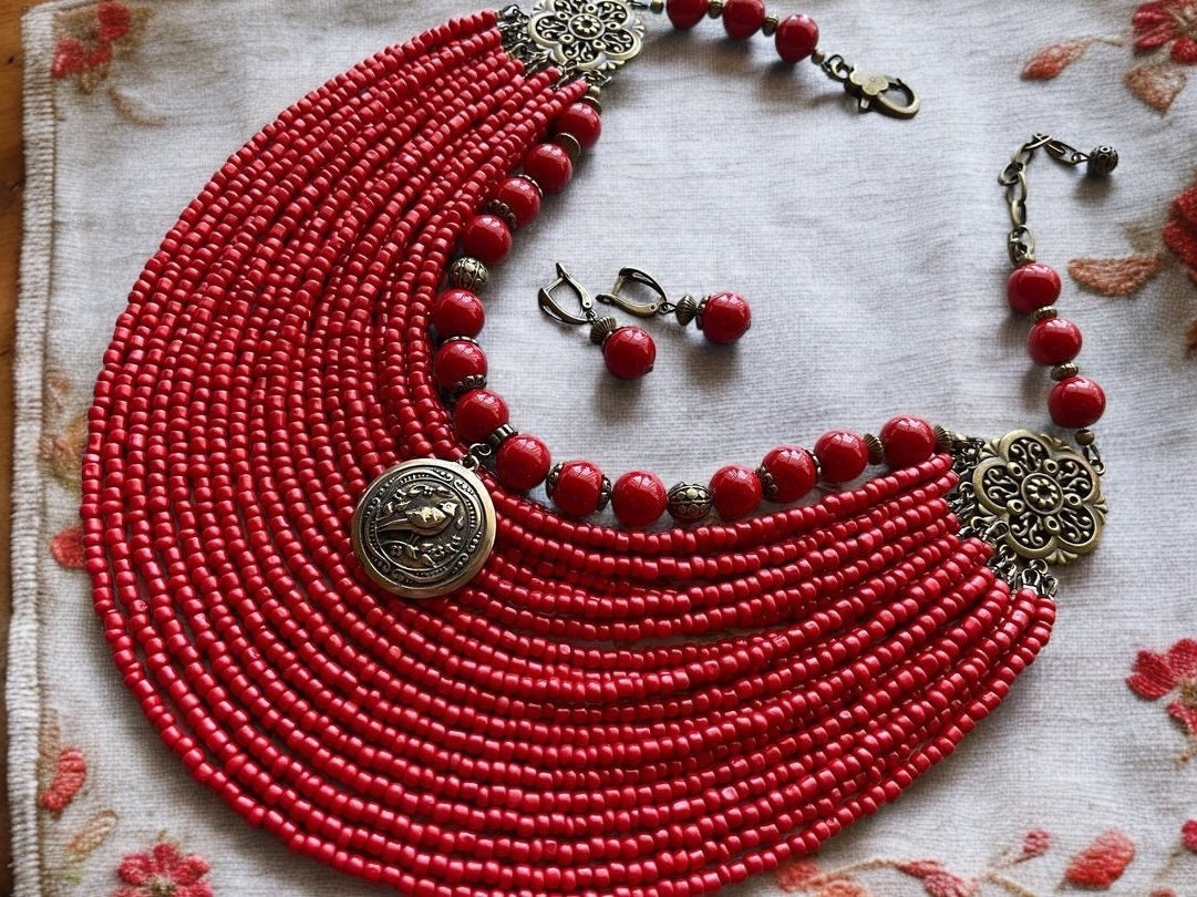 A set of red beaded necklace and earrings with brass pendant and large glass beads, displayed on a fabric surface.