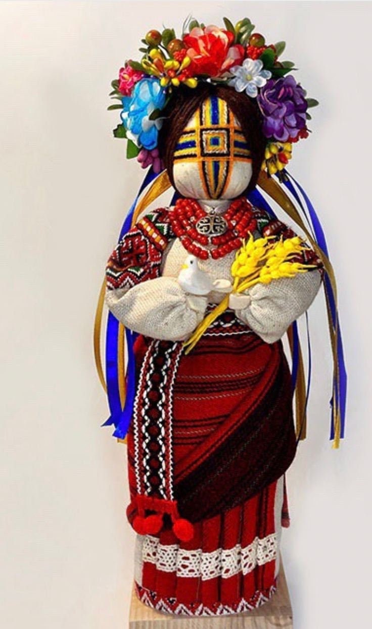 A traditional Ukrainian motanka doll, dressed in a red and black striped dress with a floral shawl, holding a blue and yellow staff, with a decorative floral crown on her head.