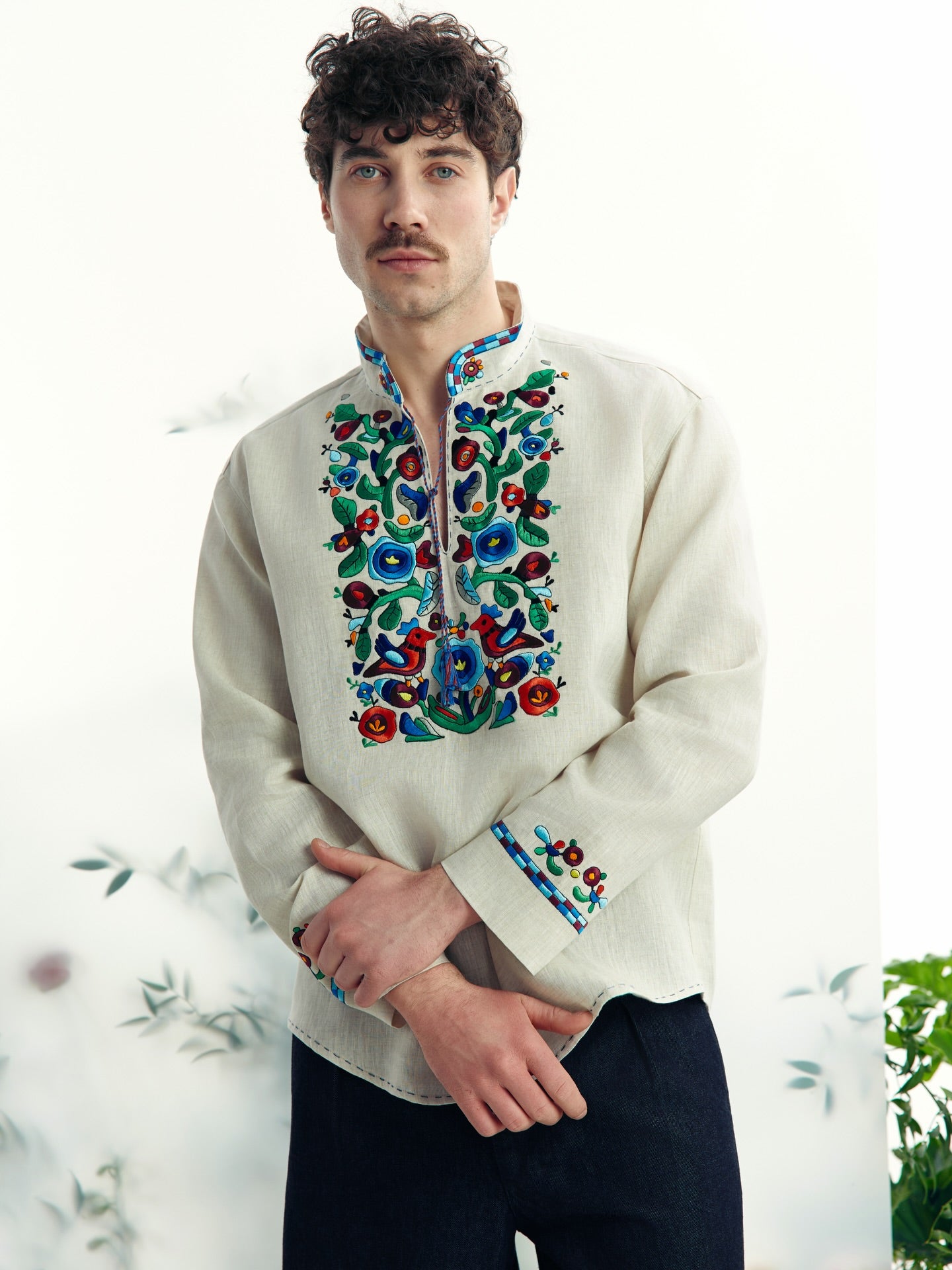 Man wearing a traditional embroidered shirt with colorful floral patterns on a white background