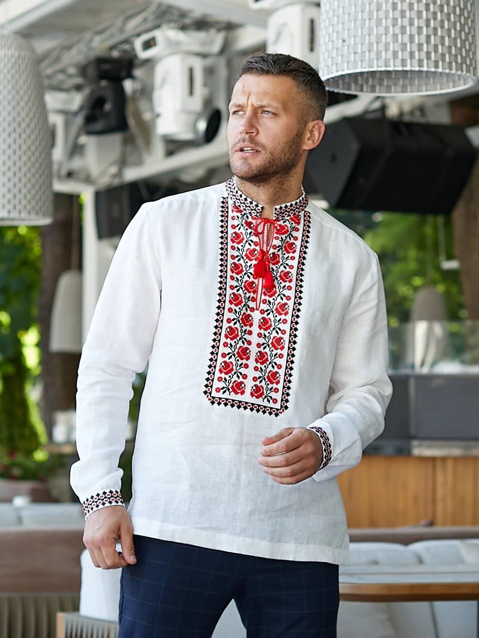 Man wearing a white embroidered shirt with red patterns in an outdoor setting