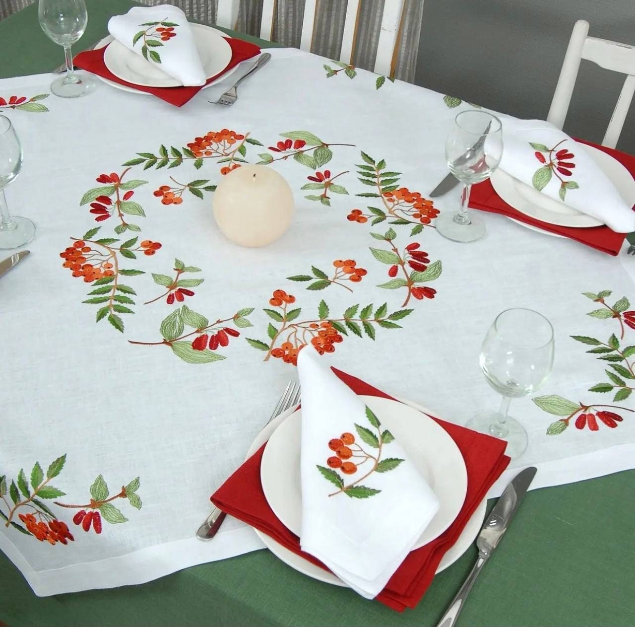 A white linen tablecloth with a floral embroidered design, accompanied by two red and white napkins, on a dining table.