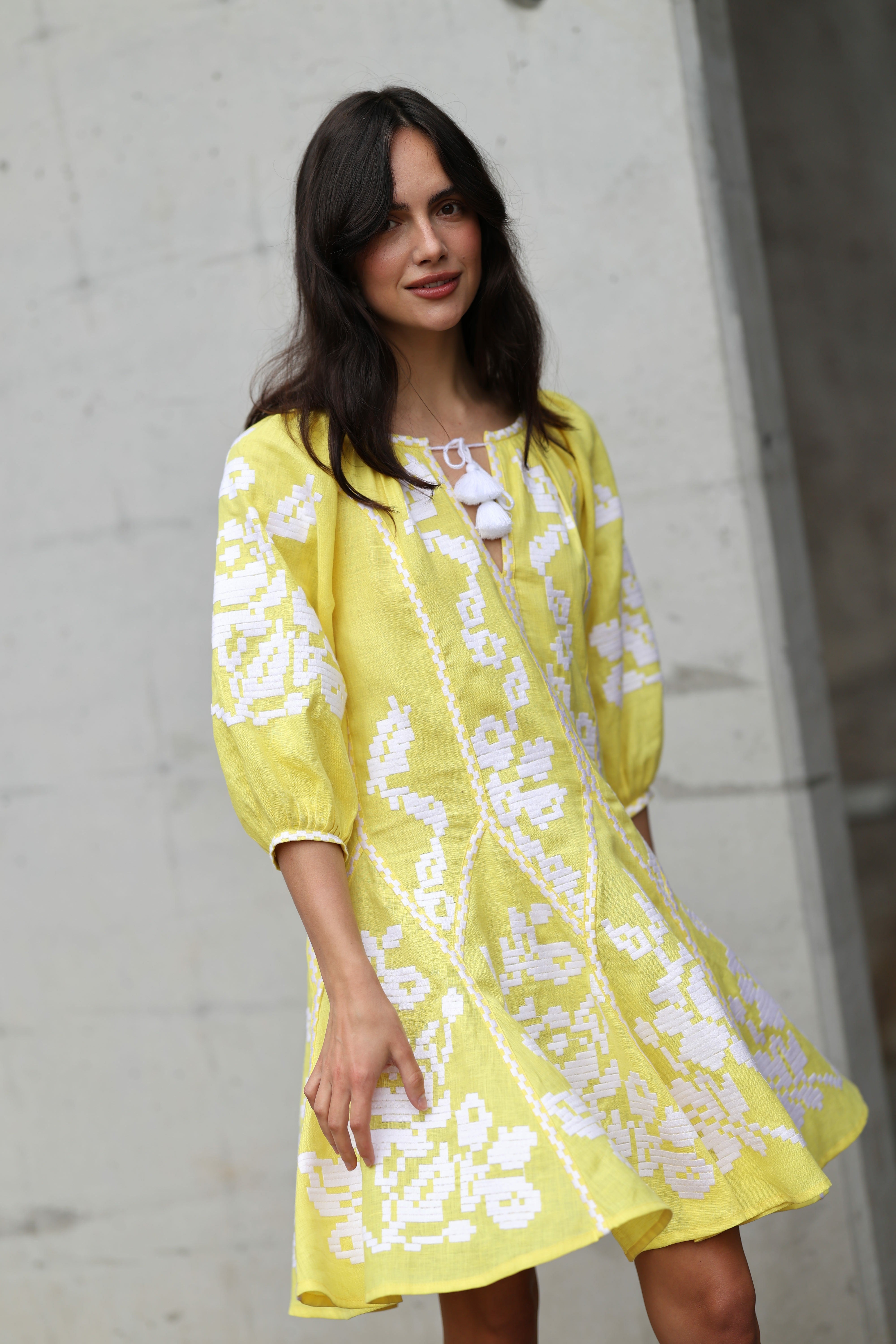Woman wearing a yellow lace dress against a concrete wall.