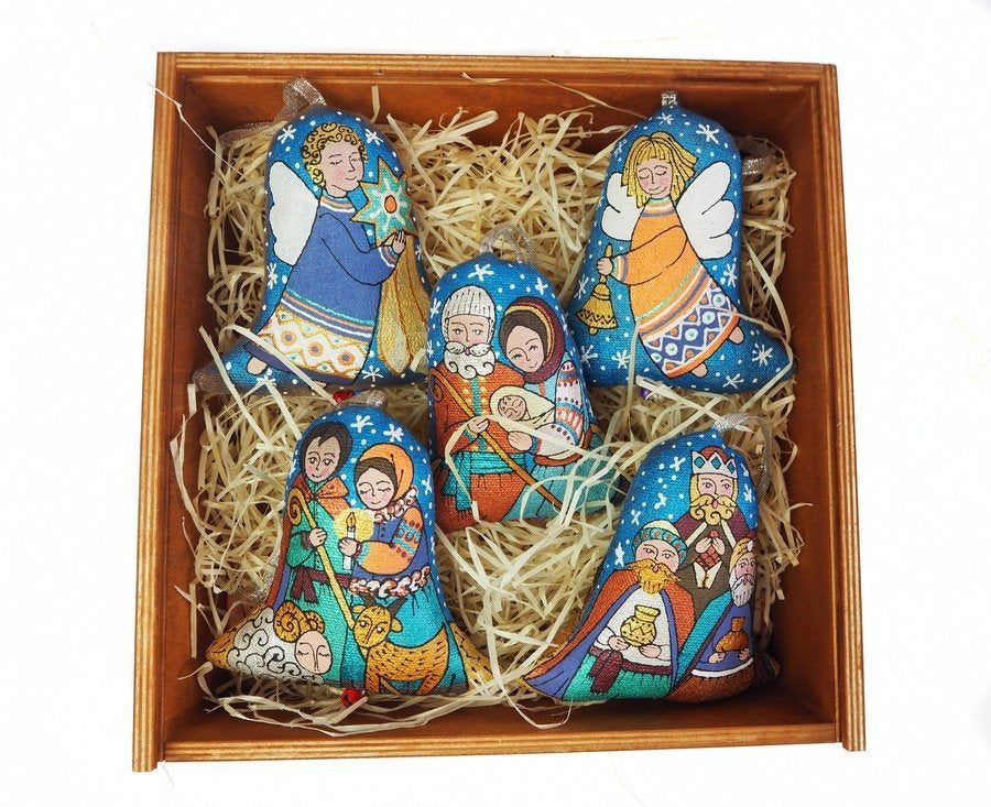 A set of embroidered Christmas tree decorations depicting characters in traditional attire, placed in a wooden box filled with straw padding.