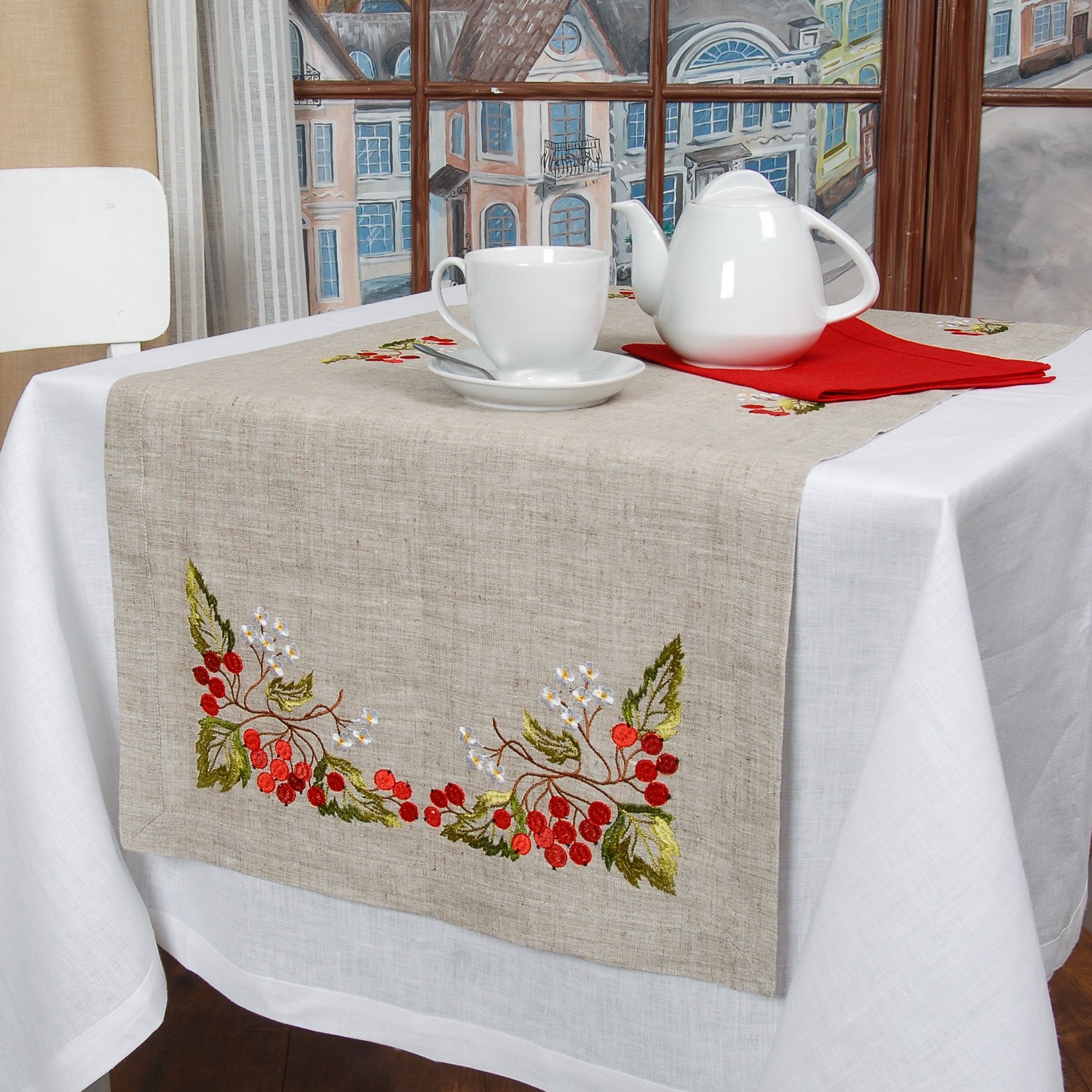 A linen tablecloth with embroidered guelder rose design, displayed on a table with tea set and red napkin.